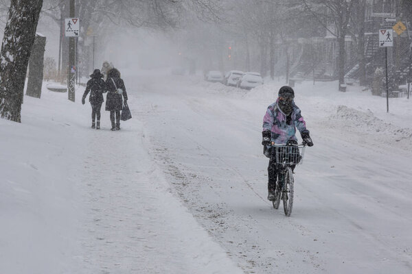 Montreal, CA, 25 February 2022: Woman riding bike on Laurier Street during snow storm