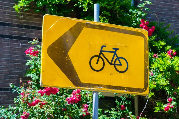 Yellow traffic sign with a bike and an arrow and red roses in background