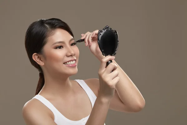 Female asian applying eye liner with mirror