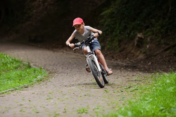 Menino de corrida de bicicleta através do parque verde — Fotografia de Stock