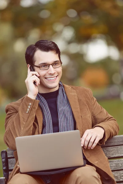 Positive Young Man Multi-Tasking In The Park — Stock Photo, Image