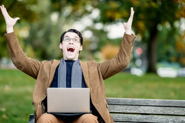 Jeune homme célébrant avec ordinateur portable sur le banc du parc — Photo