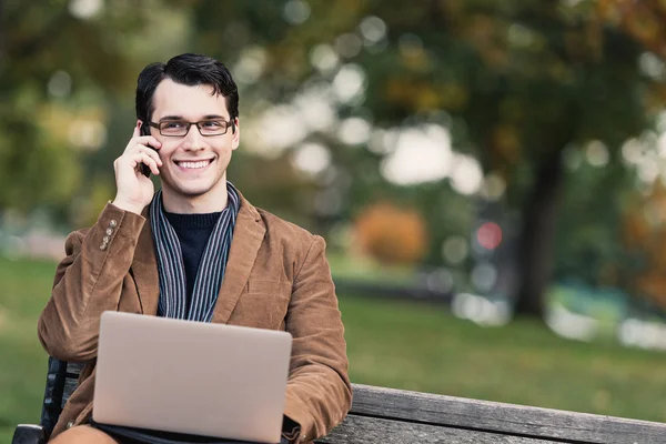 Positive Young Man Multi-Tasking In The Park — Stock Photo, Image