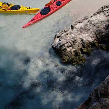 Yellow and red sea kayaks ready on the sea by the rock