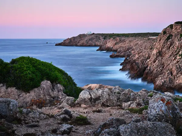 The rocky coast of Menorca island and the house at the end of the cliff, Spain