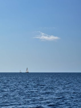 A small sailboats at sea on the horizon and a cloud