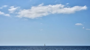 A small sailboat at sea on the horizon and a cloud