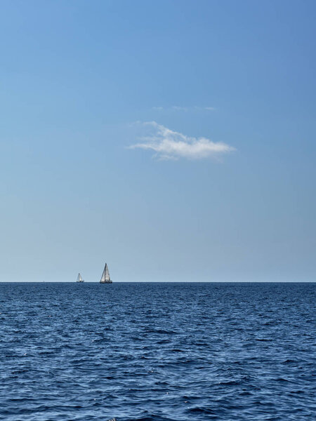 A small sailboats at sea on the horizon and a cloud
