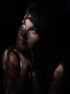 Portrait of a young woman in the dark with partial natural light through the window