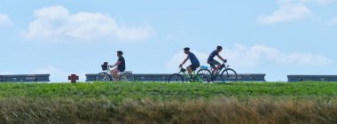 Gün boyunca bir kadın ve iki adamın bisiklet sürdüğü bir panorama.