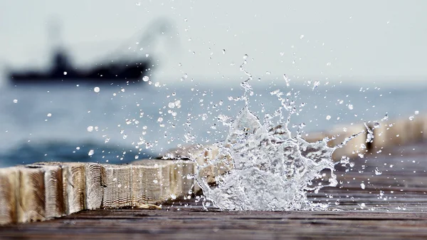 Wooden pier leading into the blue sea and the cascade of sea spr — Stock Photo, Image