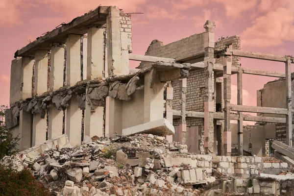 A ruined building without a roof with a void between the supporting pillars. There is a pile of bricks and concrete in front of the building.