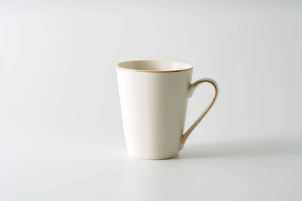 A white mug with a golden rim on top and a stripe on the handle on a white background. Copy space.