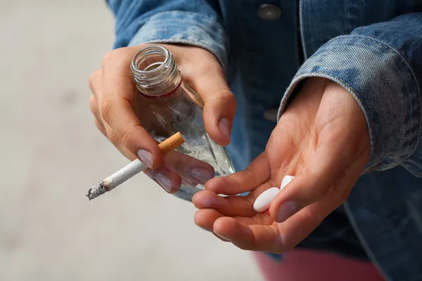 Chica sosteniendo vodka, pastillas y cigarrillos —  Fotos de Stock