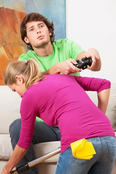 Woman cleaning the house and her husband with console — Stock Photo, Image