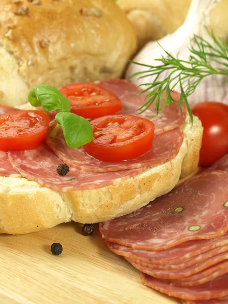 Close-up of bun with slice of ham, tomato and basil. — Stock Photo, Image