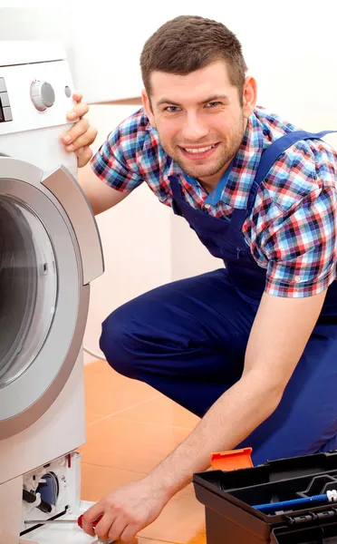 Handyman em uniforme azul que fixa uma máquina de lavar roupa — Fotografia de Stock