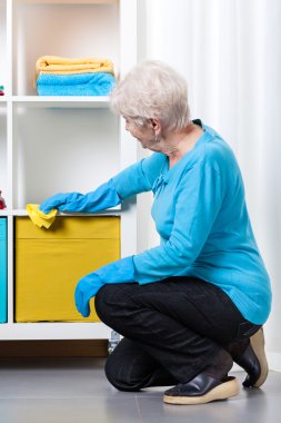 Elderly woman during dusting furniture clipart