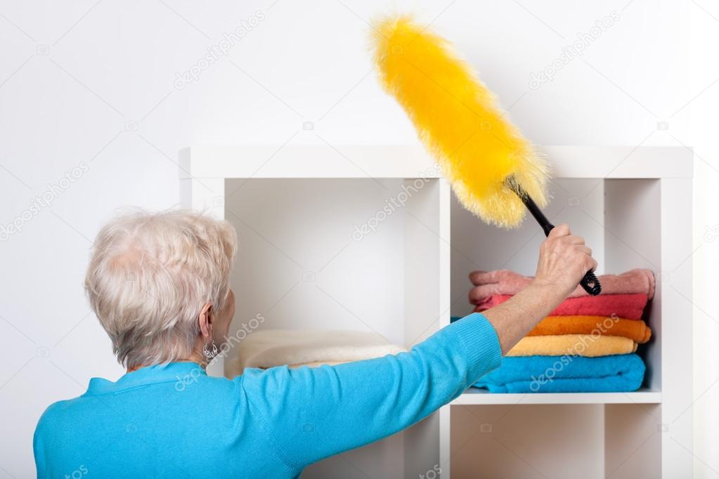Elderly lady during dusting furniture