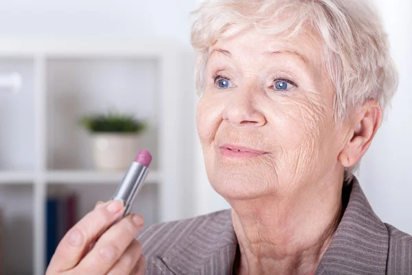 Elderly woman putting on lipstick — Stock Photo, Image