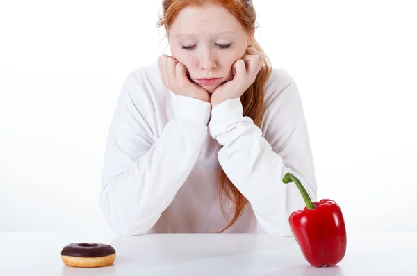 Girl choosing between doughnut and red peppers — Stock Photo, Image