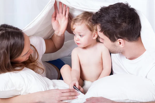 Pais amorosos com bebê triste na cama — Fotografia de Stock