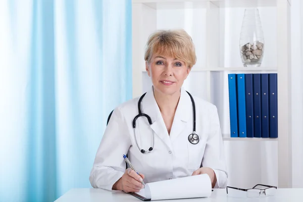 Médecin en blouse de laboratoire avec stéthoscope prenant des notes — Photo