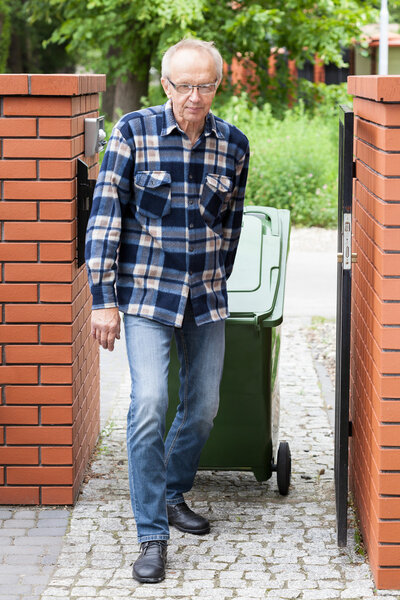 Elderly man pulling a wheeled dumpster