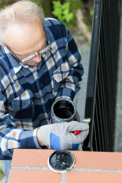 Gray-haired man painting modern metal gate — Stock Photo, Image