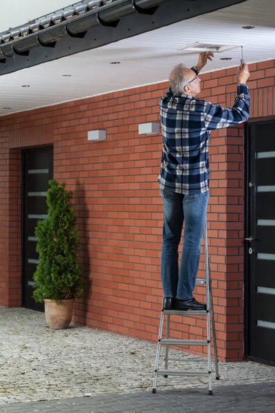 Homem em pé na escada e apertando a grade de ventilação — Fotografia de Stock