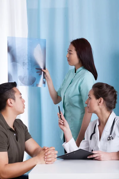 Female doctor analyzing x-ray of her Asian patient — Stock Photo, Image