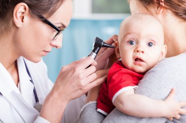 Doktor çocuğu otoskopla muayene ediyor.