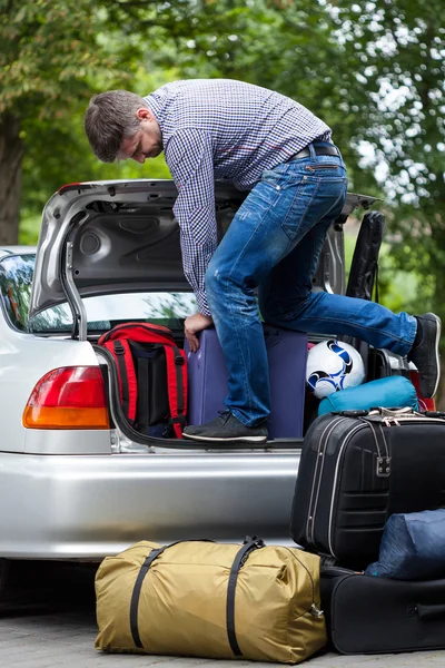 Человек, использующий свои силы, чтобы упаковать багаж в машину — стоковое фото
