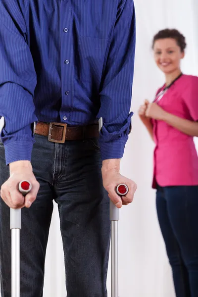 Nurse watching disabled man on crutches — Stock Photo, Image