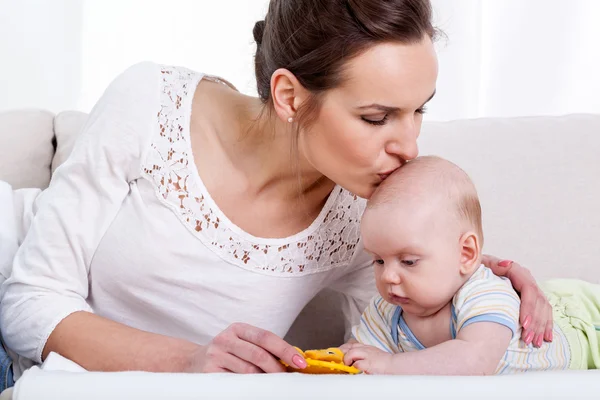 Mãe beijando bebê no sofá — Fotografia de Stock