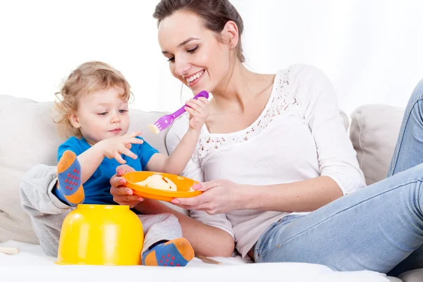 Mother feeding child on sofa — Stock Photo, Image