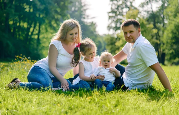 Glad familj gitting på gräset i parken — Stockfoto