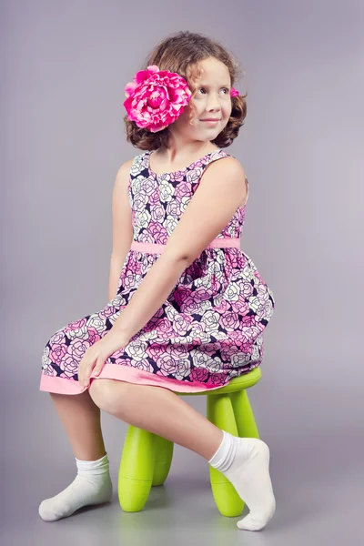 Linda chica con una flor rosa en el pelo sentado en una silla verde — Foto de Stock