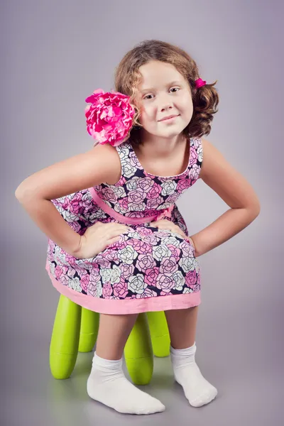 Adorable chica con una flor rosa en el pelo sentado en una silla verde — Foto de Stock