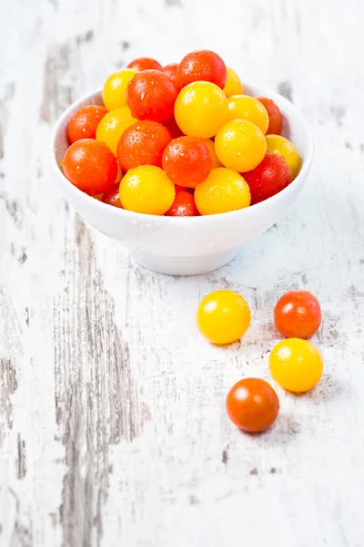 Rote und gelbe frische Kirschtomaten mit Wassertropfen in weißer Schüssel auf Holztisch — Stockfoto