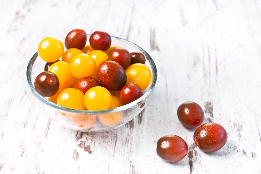 Brown and yellow fresh cherry tomatoes with water drops in glass bowl on wooden table