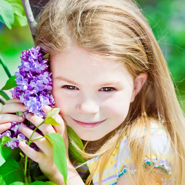 Pretty smiling blond little girl with blooming lilac — Stock Photo, Image