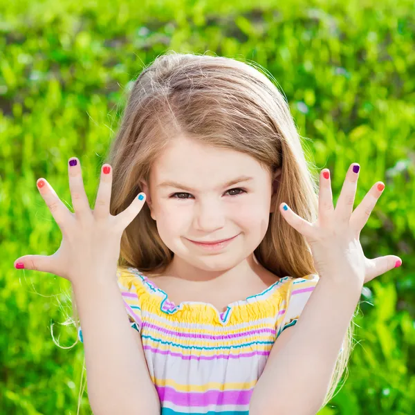 Ładny, uśmiechając się blond dziewczynka z różnobarwnych manicure — Zdjęcie stockowe