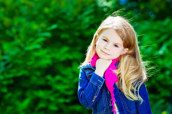 Outdoor portrait of a beautiful blond little girl wearing a jeans jacket and a pink scarf — Stock Photo, Image