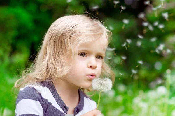 Lovely little blond little girl blowing a dandelion and making a wish in summer day — Stock Photo, Image
