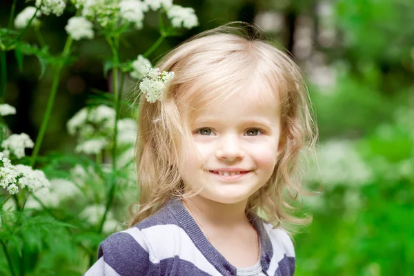 Adorable niña rubia sonriente con flor en el pelo en el día de verano —  Fotos de Stock