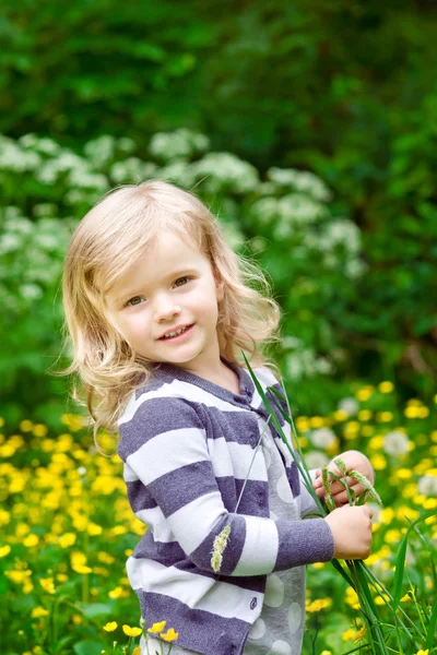 与花在她美丽的微笑金发小女孩手在夏季的一天 — 图库照片