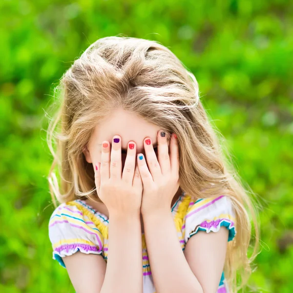 Hermosa niña rubia sonriente con el pelo largo y manicura de muchos colores que cubre sus ojos con sus manos — Foto de Stock