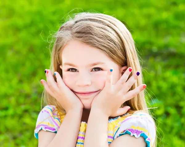 Adorabile sorridente bambina bionda con i capelli lunghi e manicure multicolore Foto Stock Royalty Free