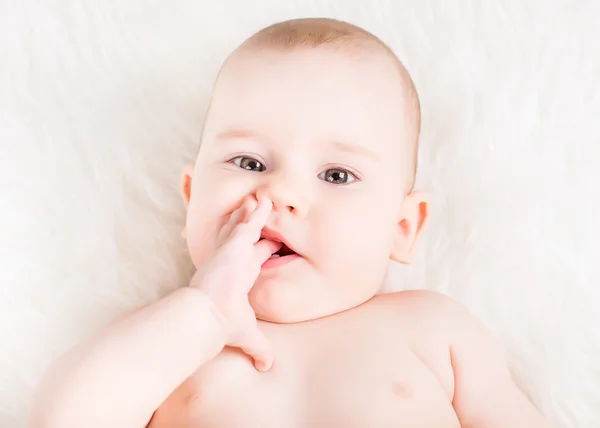 Nahaufnahme Porträt eines schönen Babys, das auf weißem Fell liegt und Finger lutscht — Stockfoto